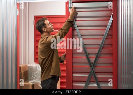Man opening door of self-storage unit to place boxes with belongings inside Stock Photo