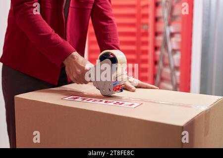 Hands of man taping moving boxes with fragile belongings Stock Photo