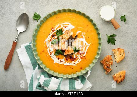 Pumpkin and carrot cream soup with herbs, seasonings and seeds in bowl on gray concrete table background in rustic style. Thanksgiving traditional aut Stock Photo