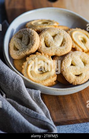From above fresh homemade baked butter cookies placed in a bowl on a wooden cutting board beside a gray napkin, set against a minimalist concrete back Stock Photo