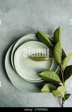 A serene composition featuring fresh green cherry leaves resting on muted ceramic plates against a textured grey background Stock Photo
