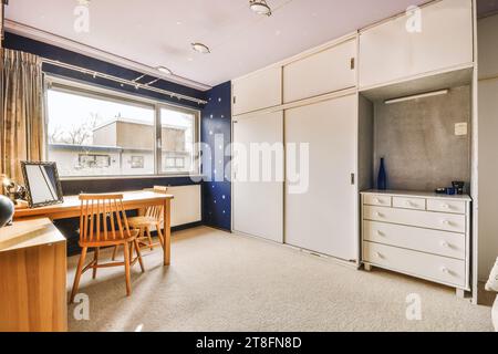 Wooden chair and desk in spacious home office with wardrobe and large window in contemporary apartment Stock Photo