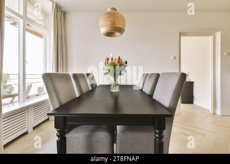 Flower vase on black dining table with chairs arranged by large window in contemporary dining room at home Stock Photo