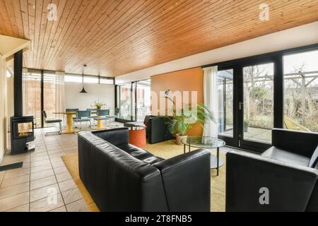 Black leather sofas and coffee table placed next to bright window in spacious living room with dining zone in background Stock Photo