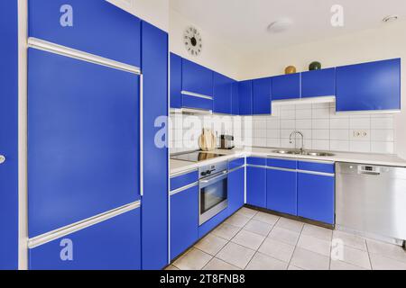 Interior of spacious kitchen with blue cabinets and modern appliances at contemporary house with white tiles Stock Photo
