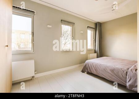 Interior of spacious bedroom with comfortable bed and bright windows in modern house with grey walls Stock Photo