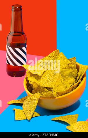 A vibrant still life image featuring a bowl of crunchy nacho chips beside a dark bottle against a split background of red and blue Stock Photo
