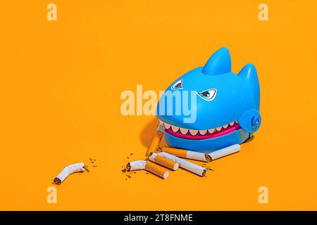 High angle of blue shark toy amidst scattered cigarette butts on a yellow background Stock Photo