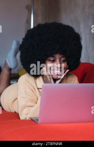 Front view of young cheerful African American female with Afro hairstyle with his hands on his face while looking at the computer while resting on com Stock Photo