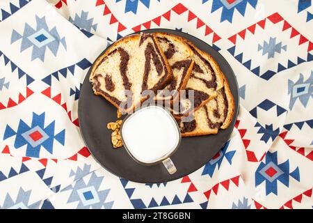 Cozonac, Romanian traditional sweet bread with walnut filling, sliced on a black plate and patterned cloth, flat lay Stock Photo