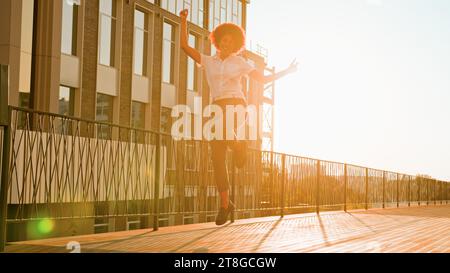 Female silhouette in sunshine city outdoors urban happy carefree winner African American business woman walking jumping celebrate win achievement Stock Photo