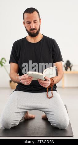 Caucasian guy with beard looking and reading book of mudras. Concentrated middle-aged man Stock Photo