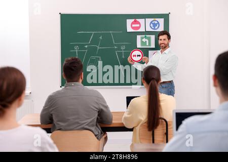 Teacher showing No Overtaking road sign to audience near chalkboard in driving school Stock Photo