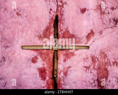 An iron brace on a pink wall intended to stabilize a crack in the town of Oia takes on the shape of a cross. Stock Photo