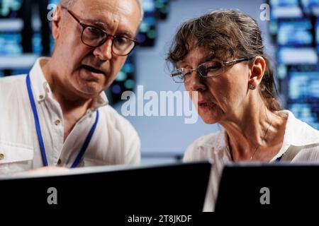 Efficient workers monitoring rackmounts, optimizing them for data processing requirements of AI applications. Precise employees working in cloud computing business used for neural network training Stock Photo