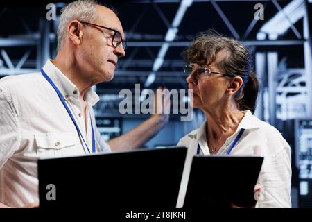 Old developers performing diagnostic assessments on server clusters to detect problems with data center equipment. Programmers crosschecking maintenance lists, examining for potential system hiccups Stock Photo