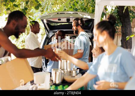 Diverse group distributing donation boxes to those in need at a shelter of homeless individuals and refugees. Charity workers sharing necessities and offer assistance through a non-profit food bank. Stock Photo