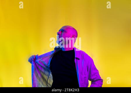 Bearded, bald man opening his shirt. Isolated on yellow background. Stock Photo