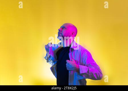 Bearded, bald man opening his shirt. Isolated on yellow background. Stock Photo