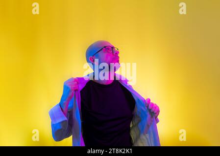 Bearded, bald man with glasses opening his shirt. Isolated on yellow background. Stock Photo