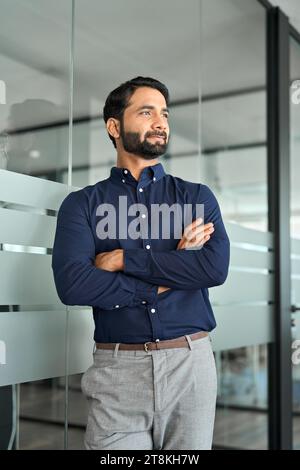 Thoughtful Indian business man looking away standing arms crossed in office. Stock Photo