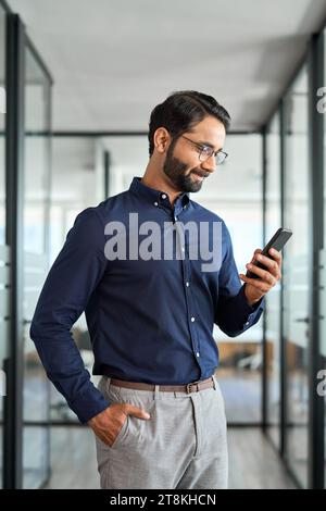 Indian business man employee using mobile phone standing in office. Stock Photo