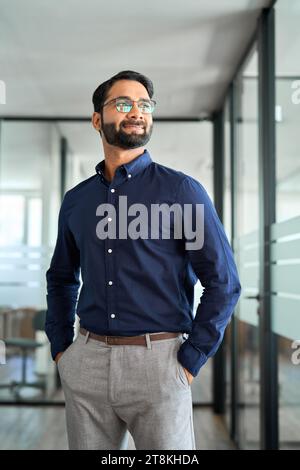 Confident happy Indian business man leader looking aside standing in office. Stock Photo