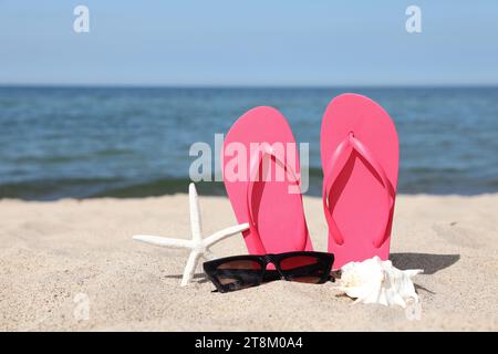 Stylish pink flip flops, sunglasses, starfish and seashell on beach sand, space for text Stock Photo
