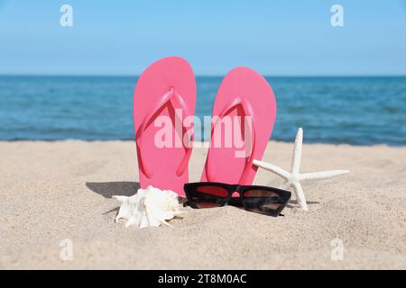 Stylish pink flip flops, sunglasses, starfish and seashell on beach sand Stock Photo
