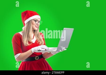 young blonde woman in glasses dressed as santa claus typing on a laptop Stock Photo