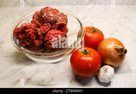 fresh ground beef in glass bowl with vegetables and kitchen ingredients in background on kitchen counter Stock Photo