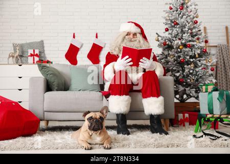 Santa Claus with book and cute French bulldog in room decorated for Christmas Stock Photo