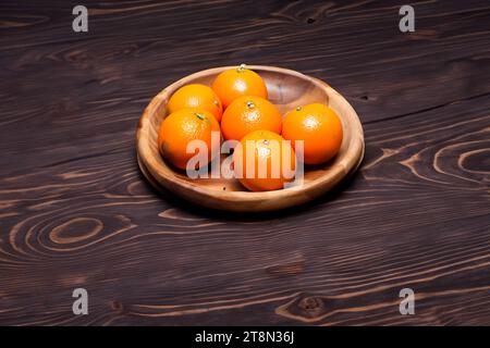 Tangerines in a wooden bowl on a dark wooden background. Stock Photo