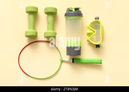 Badminton racket with sports bottle, dumbbells and swimming goggles on yellow background Stock Photo