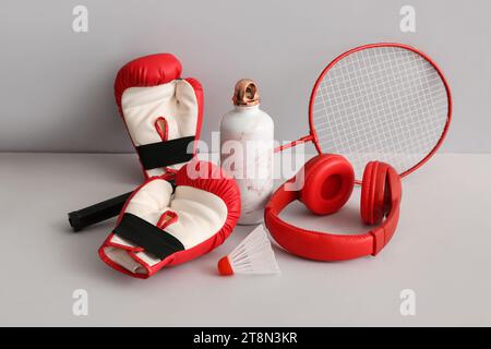 Badminton racket with shuttlecock, boxing gloves, headphones and sports bottle on grey background Stock Photo