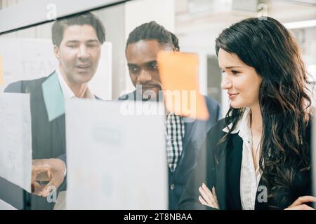 A diverse group of professionals meets in the office, using stick notes on a glass board to Stock Photo