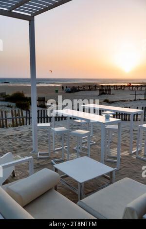 White tables and chairs in the sand, lounge bar, beach bar with a view of the sunset by the sea, Tarifa, Strait of Gibraltar, Costa de la Luz Stock Photo