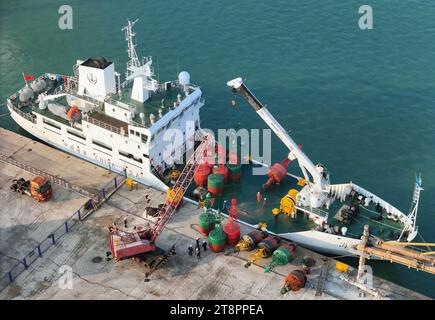 YANTAI, CHINA - NOVEMBER 21, 2023 - At Longkou Port in Shandong province, a crane loads a navigation mark onto the 'Haixun 153' navigation mark ship, Stock Photo