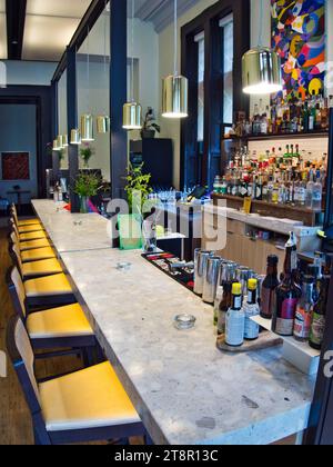 View along a white stone bar top in an upscale historic hotel with well-stocked bar. Yellow chairs, colorful art, and mood lighting. Stock Photo