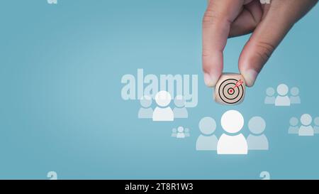 Human hand holds a dart board icon drawn on a wooden block and connects to a target customer on a light blue background It represents the selection of Stock Photo