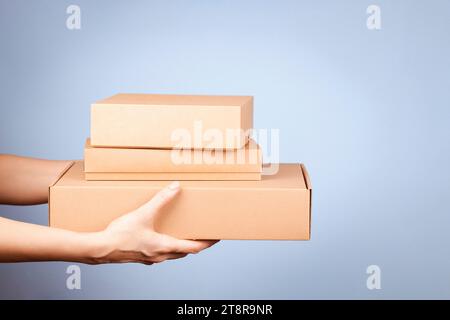 Stack of different size cardboard boxes in female hands. Blank brown parcel boxes on light blue background. Packaging, shopping, free shipping Stock Photo