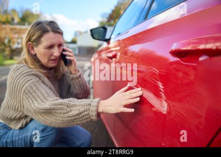 Unhappy Mature Female Driver With Damaged Car After Accident Calling Insurance Company On Mobile Phone Stock Photo