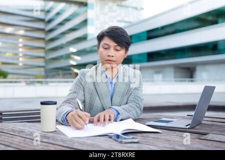Asian business specialist man at laptop takes notes outdoor Stock Photo