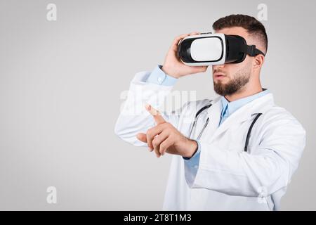 Young male doctor in white coat using VR glasses, grey background Stock Photo