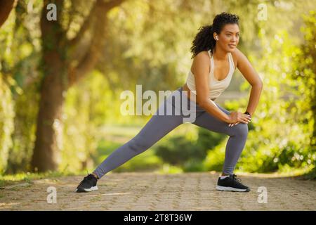 Sportswoman with earbuds exercising doing deep side lunge stretching outdoors Stock Photo