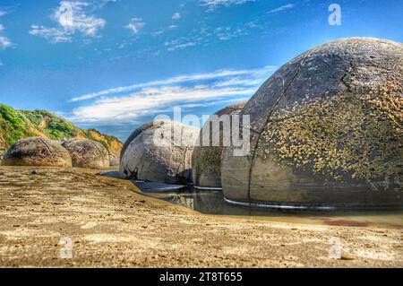 Moeraki Boulders. HDR, The Moeraki Boulders / Kaihinaki are unusually large spherical boulders lying along a stretch of Koekohe Beach on the wave-cut Otago coast of New Zealand between Moeraki and Hampden. They occur scattered either as isolated or clusters of boulders within a stretch of beach where they have been protected in a scientific reserve. These boulders are grey-colored septarian concretions, which have been exhumed from the mudstone and bedrock enclosing them and concentrated on the beach by coastal erosion Stock Photo