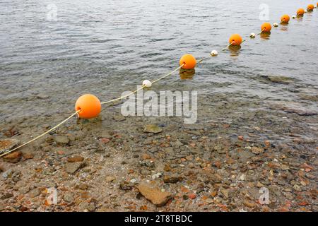 Orange spherical buoys on a rope in the sea, fencing a safe swimming area Stock Photo