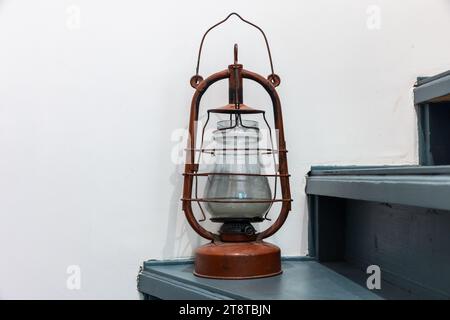 Vintage red kerosene lamp stands on green wooden stairs in front of a white wall, close up photo with selective soft focus Stock Photo