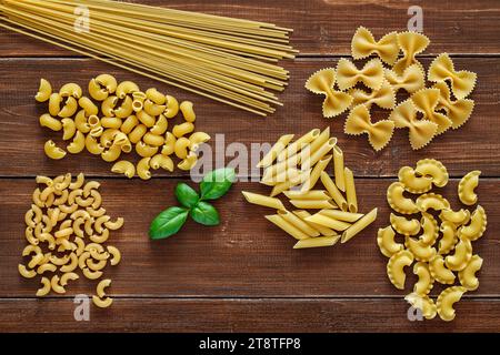 Pasta, set of raw farfalle, spaghetti, pipe rigatoni, maccheroni, penne rigate, cresta di gallo, basil leaf,  on wooden plank dark background, top vie Stock Photo