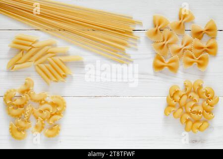 Pasta, set of raw farfalle, spaghetti, pipe, maccheroni, penne, cresta,  on white wooden board background, top view, space to copy text. Stock Photo